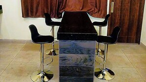 Una stanza con un tavolo nero e due sedie nere, una tenda marrone, una porta in legno e un condizionatore d'aria a parete.