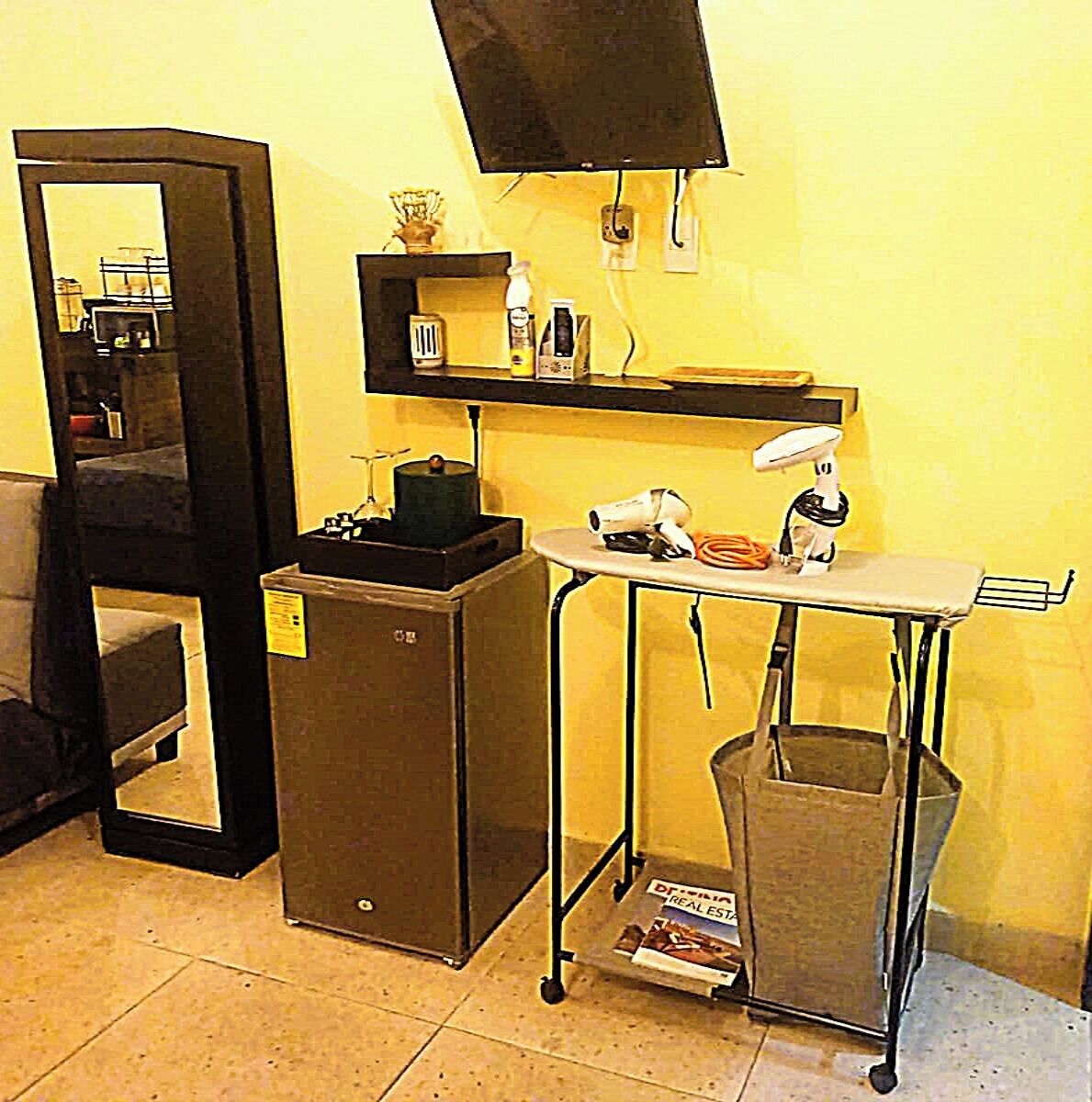 A compact room with a desk, a chair, a trash bin, and a television on a stand.