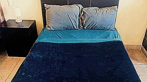 Un letto con una coperta blu scuro e un cuscino abbinato, un comodino con una lampada e un pavimento piastrellato.