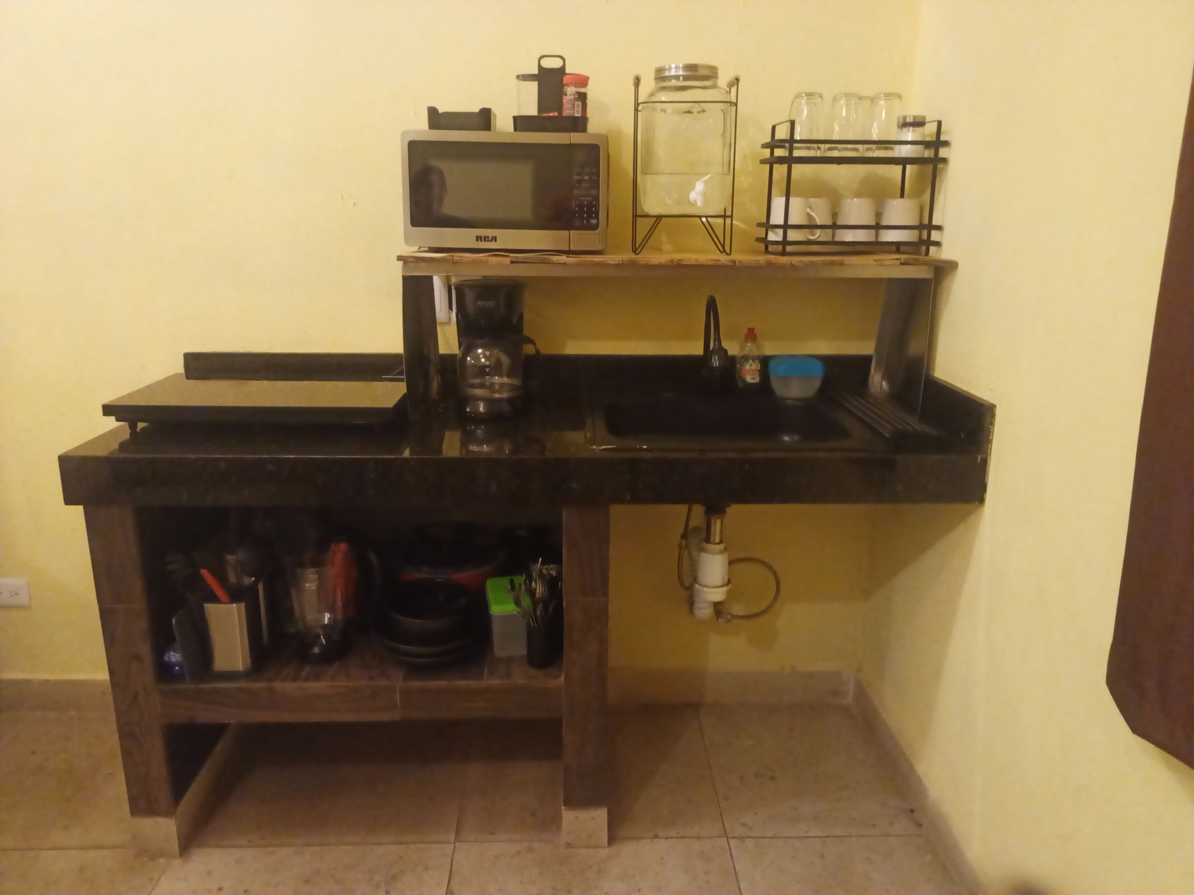 Een kleine keuken met een magnetron, koffiezetapparaat en een waterdispenser op een plank.