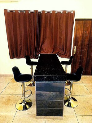 Un comedor con una mesa negra y cuatro sillas negras de bases brillantes. Cortinas marrones cuelgan sobre la mesa.