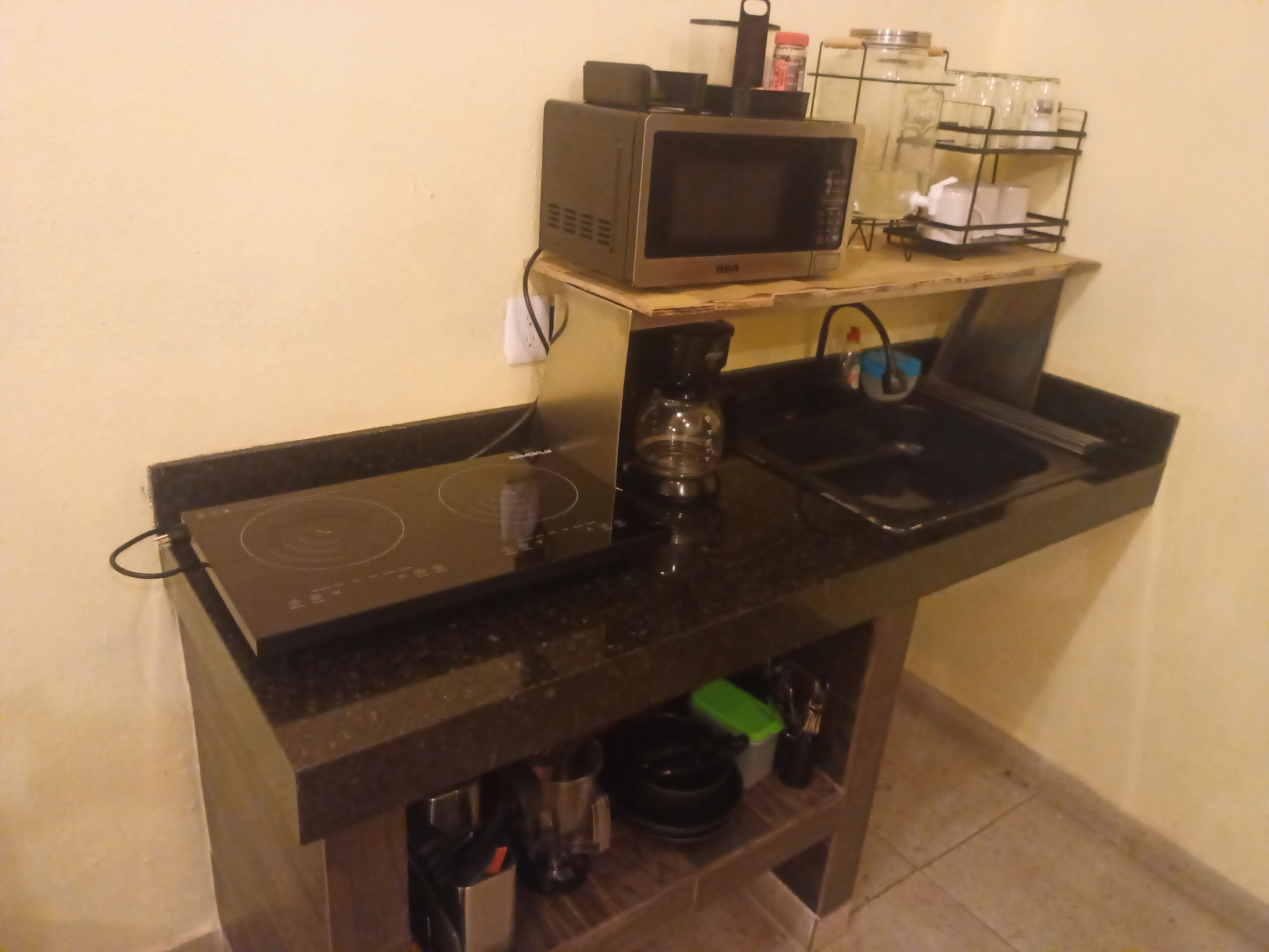 Una cocina equipada con microondas, cafetera y lavamanos.