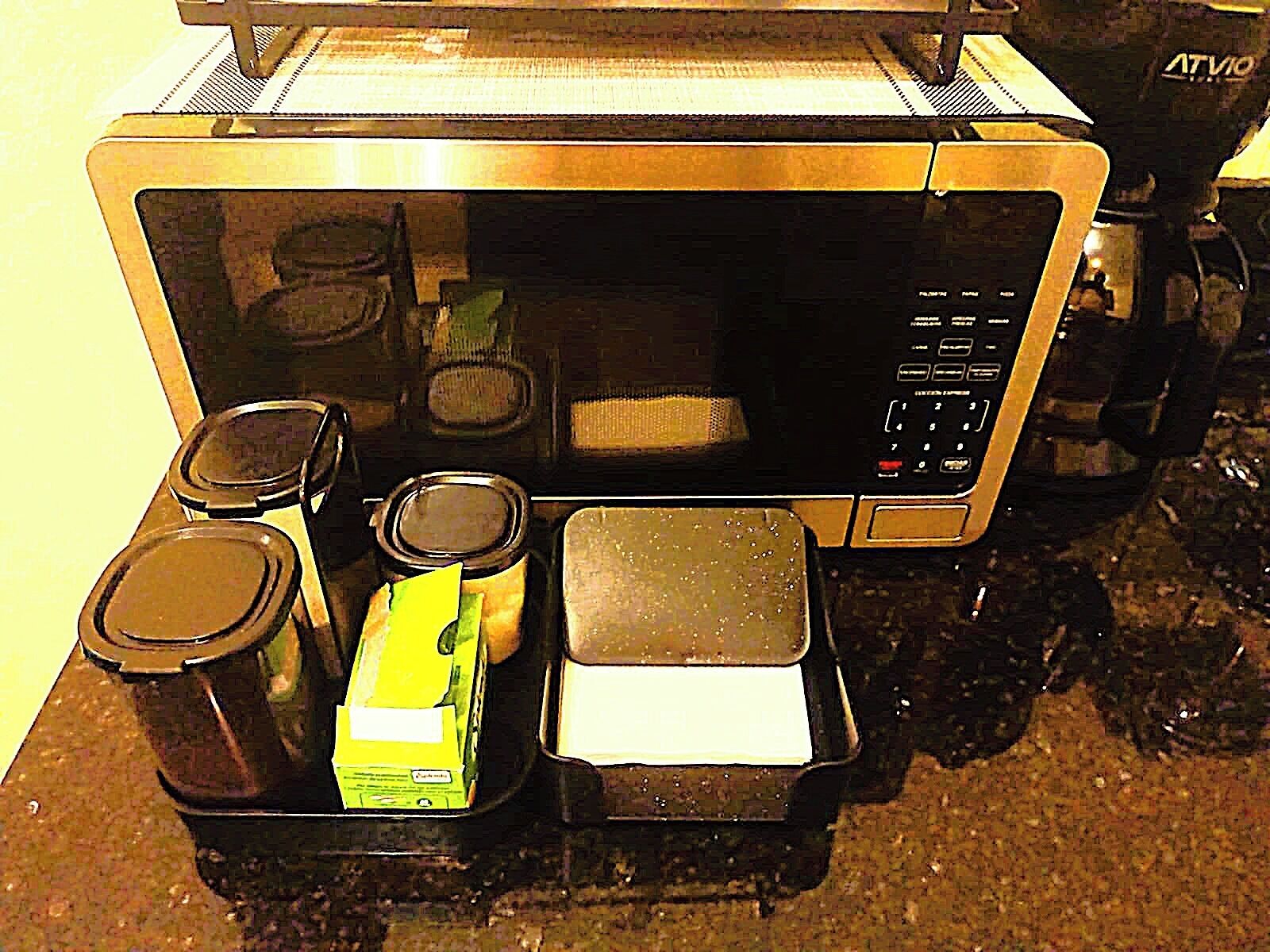 A microwave with a digital display, a coffee maker, a box of tissues, and a small container.
