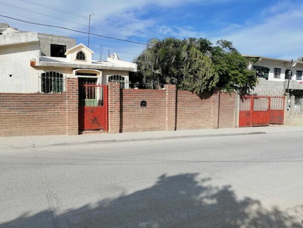 A residential building with a red gate, brick walls, and a large tree in front.