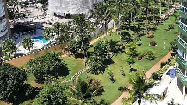 Un edificio alto con piscina y palmeras, rodeado de vegetación y vistas al océano.