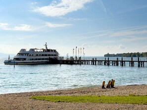Um ferry atracado em um cais com costa rochosa e uma área gramada ao primeiro plano.
