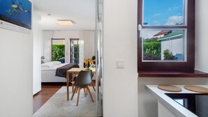 Eine moderne Küche mit Fenster, ein Essbereich mit Tisch und Stühlen sowie ein Schlafzimmer mit Bett und Nachttisch.
