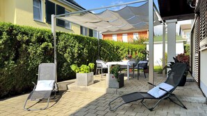 Eine Terrasse mit Tisch, Stühlen, Sonnenschirm und einer Hecke.