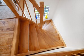 A wooden staircase with a modern design, a view of the outside through a window, and a wooden floor.