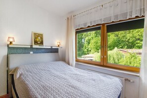 A bedroom with a bed, two bedside lamps, a framed picture, and a window with a view of greenery. - Holiday Apartment "Gabi" with Shared Terrace & Wi-Fi (Malchow)