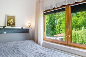 A bedroom with a bed, a window with a view of greenery, a bedside table with a lamp, and a framed picture on the wall. - Holiday Apartment "Gabi" with Shared Terrace & Wi-Fi (Malchow)