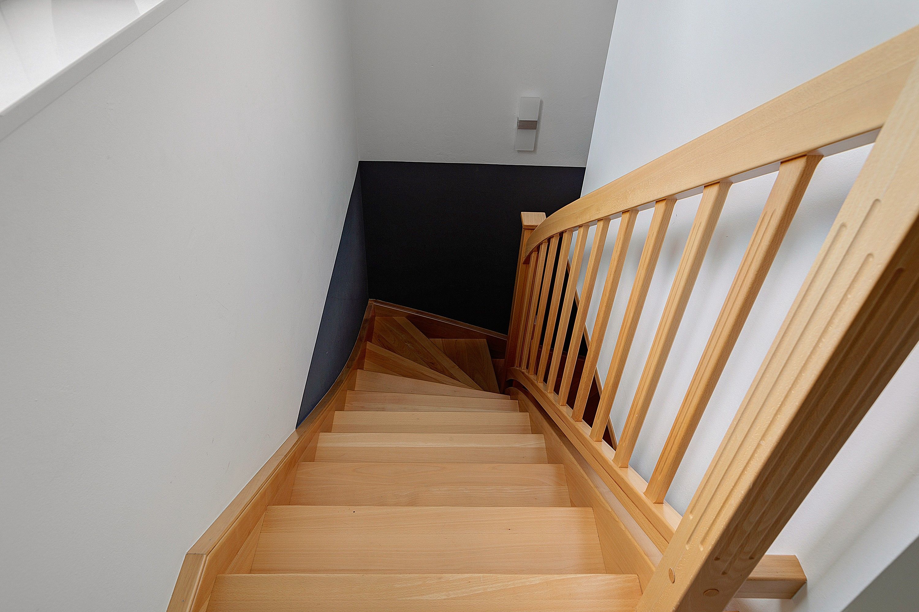 A wooden staircase with a handrail, leading to a dark-colored landing area.