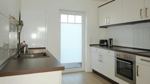 A modern kitchen with white cabinets, a stainless steel sink, and a built-in oven. - Holiday Home 'Melody' with Private Terrace and Wi-Fi (Ralswiek)