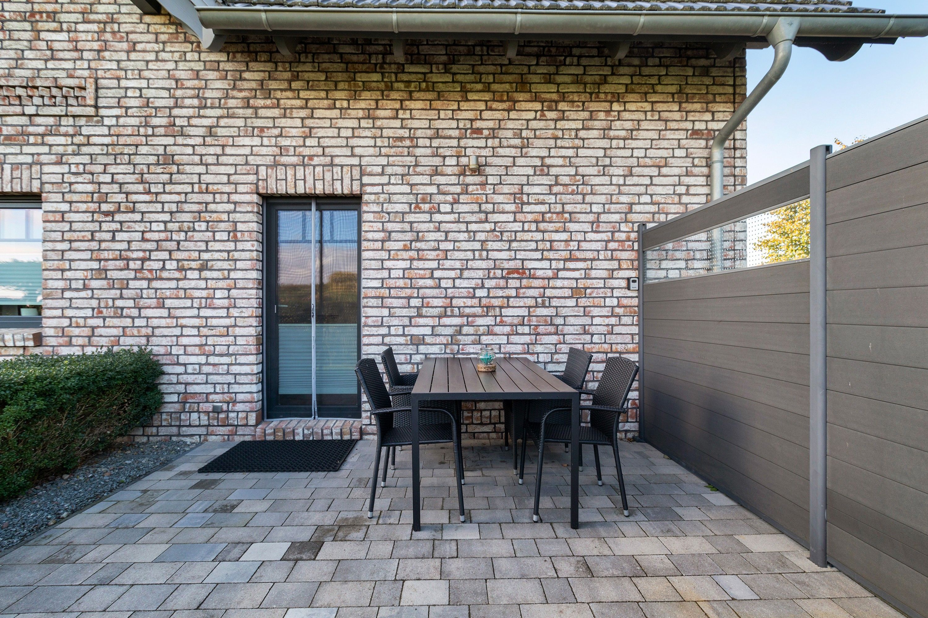 Une terrasse avec un mur en briques, une table et des chaises.