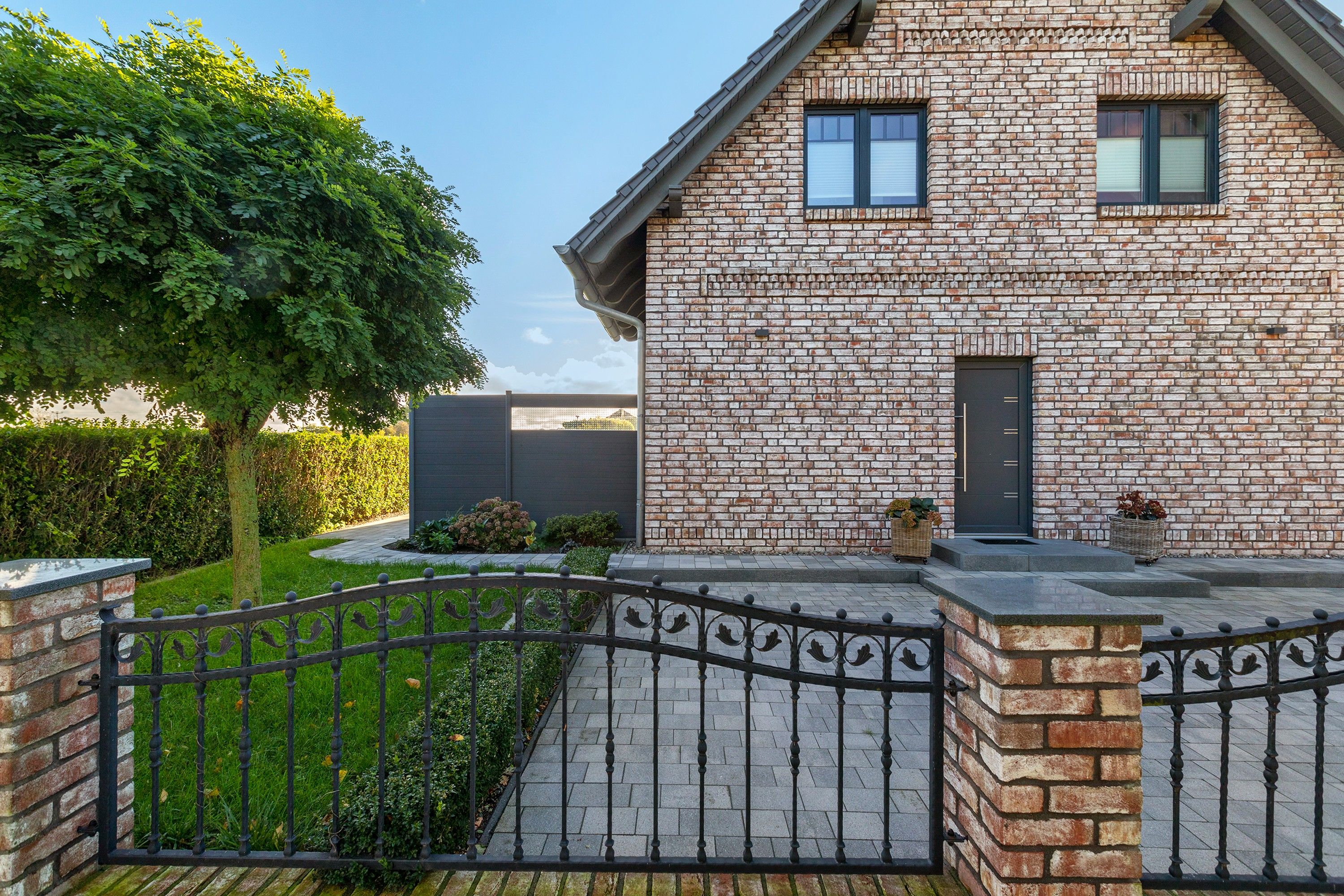 Een stenen huis met een hek, een boom en een haag.
