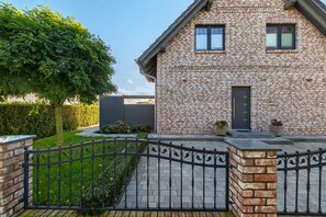 A brick house with a gated entrance, a tree, and a hedge. - Holiday Home 'Melody' with Private Terrace and Wi-Fi (Ralswiek)