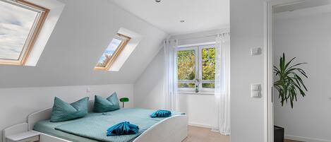 A bedroom with a bed, a nightstand, a window, and a plant.