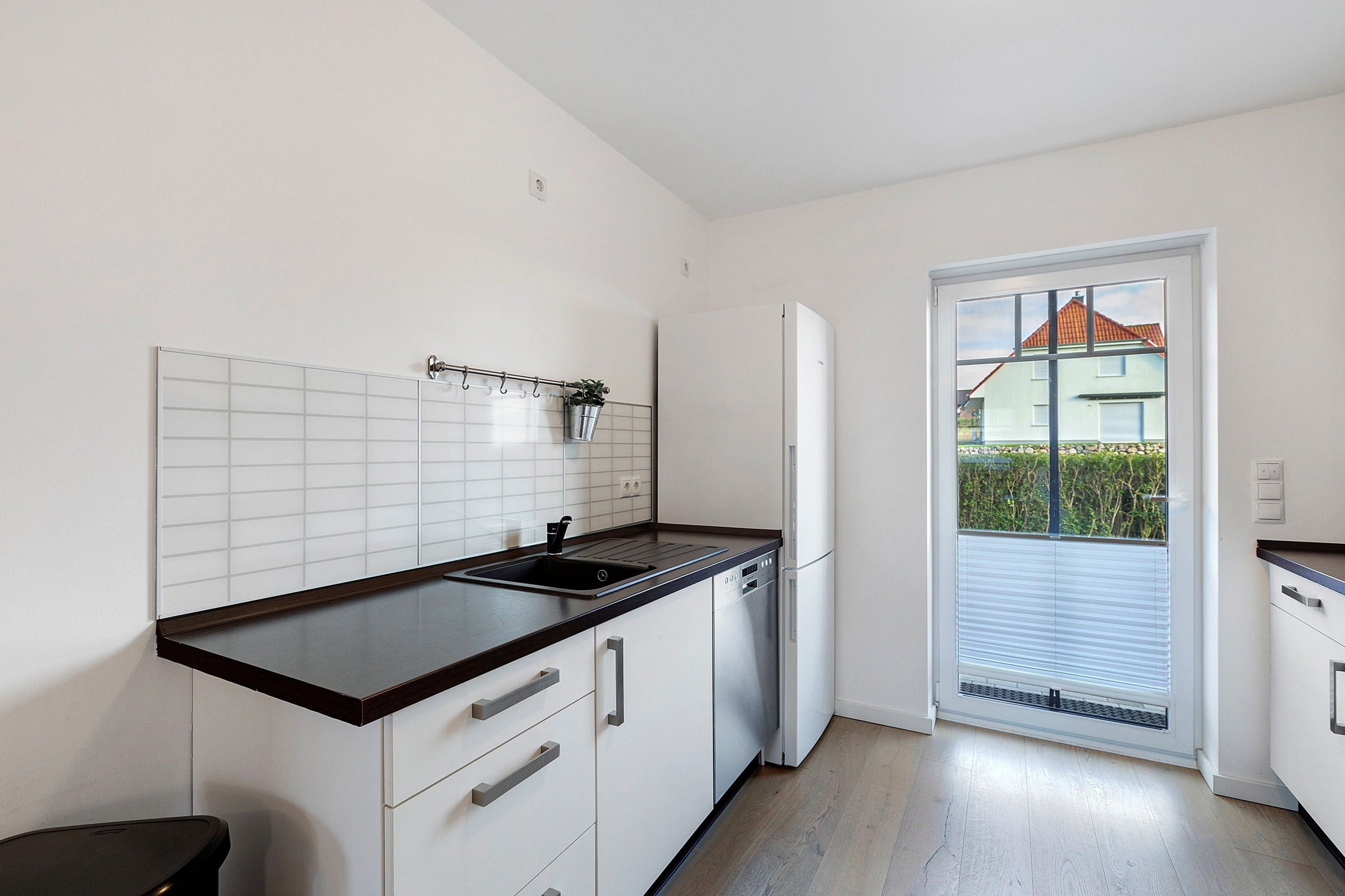 A kitchen with white cabinets, a black countertop, and a window with a view of a house.