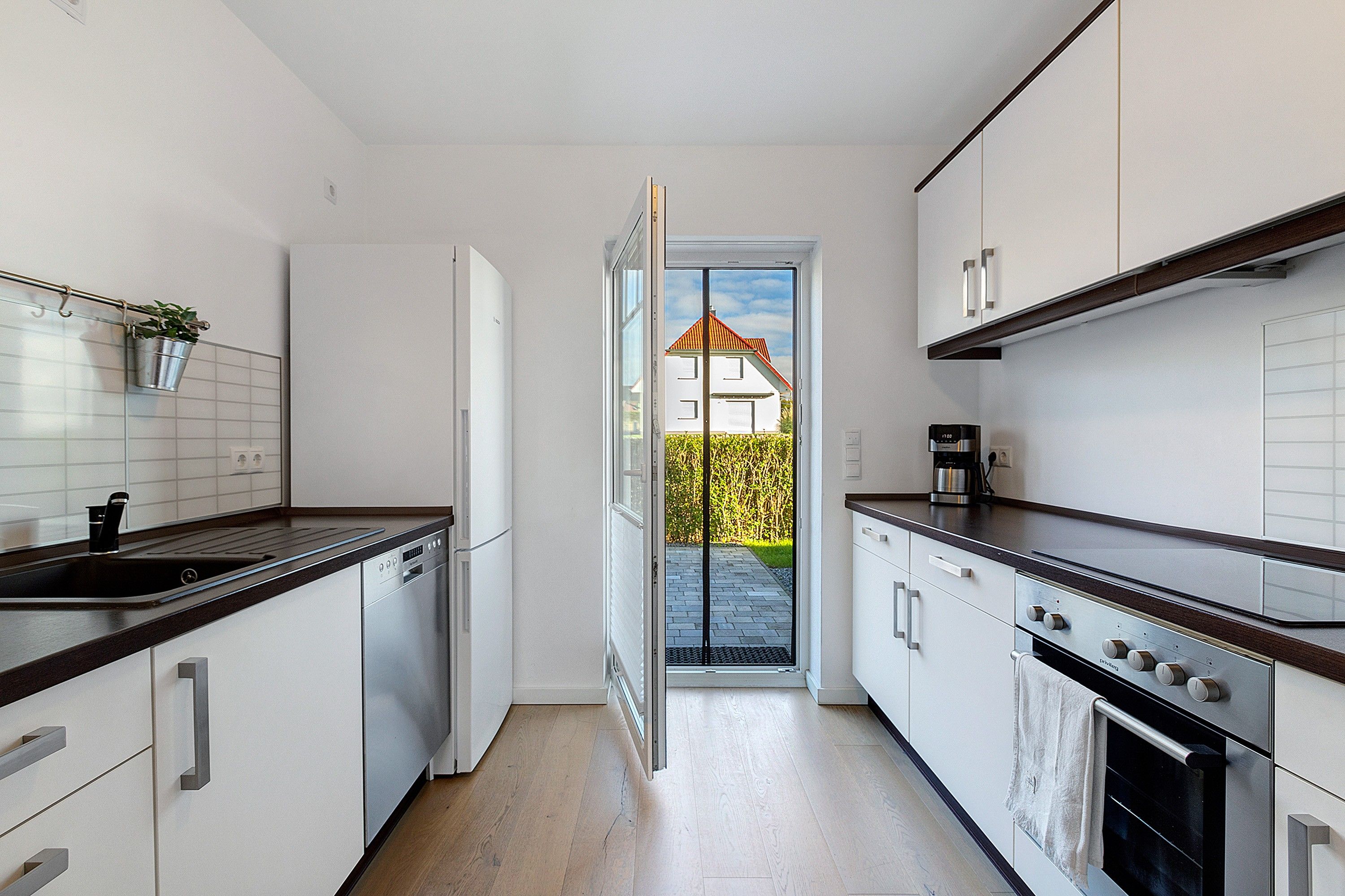 Una cocina moderna con armarios blancos, lavavajillas, estufa y cafetera.