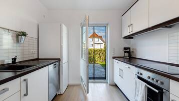 Una cocina moderna con armarios blancos, lavavajillas, estufa y cafetera.