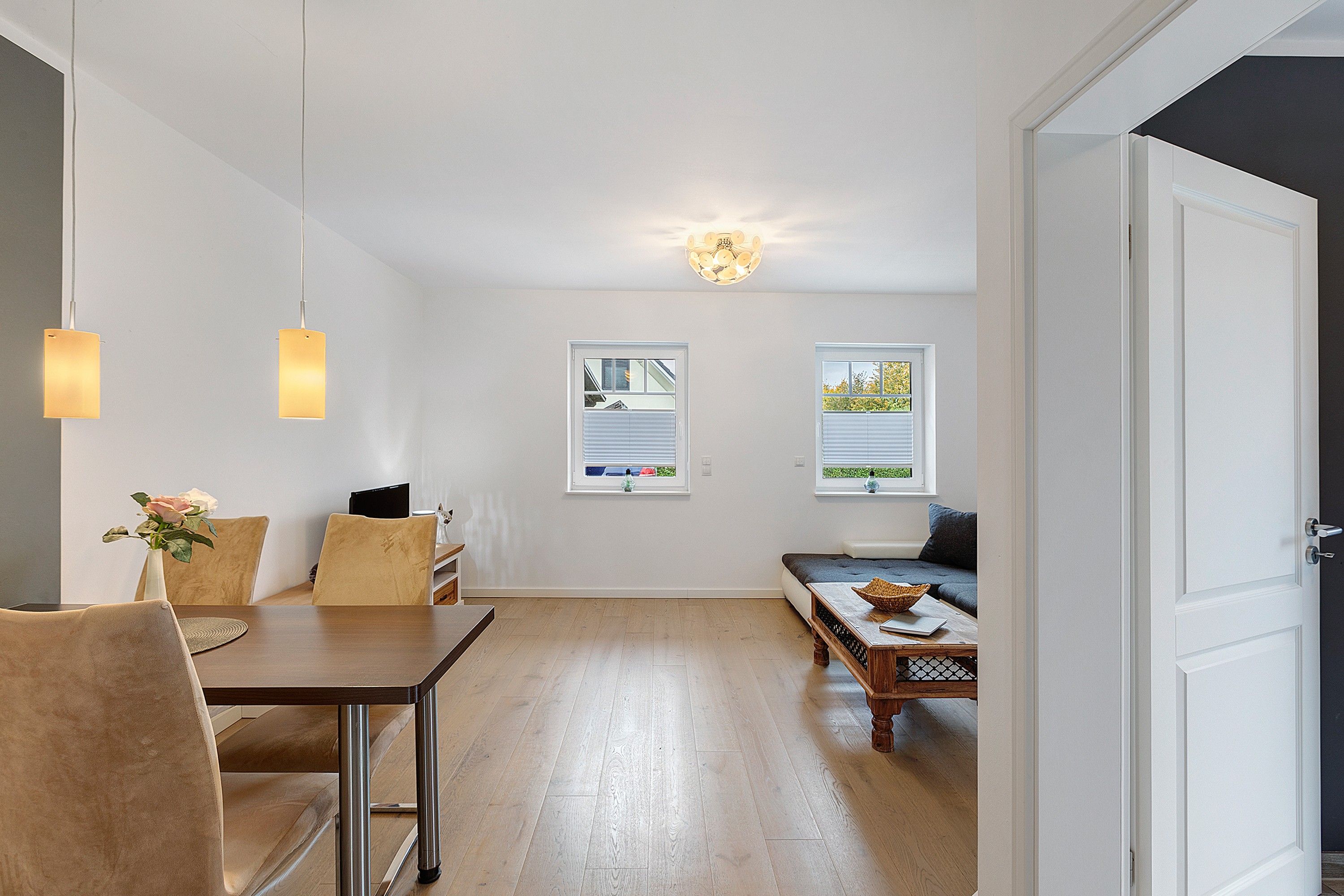 Ein modernes Interieur mit Essbereich, einer Couch und zwei Fenstern mit Blick.