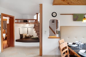 A room with a bed, a dining table with chairs, a staircase, and a wall-mounted clock. - Holiday Home 'Ferienhaus Plattner' with Mountain View, Private Terrace and Wi-Fi (Oetz)