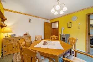A dining area with a wooden table, chairs, a lamp, a clock, and a door leading to another room.