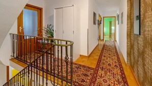 Un pasillo con escaleras de madera, alfombra estampada y una puerta que da a otra habitación.