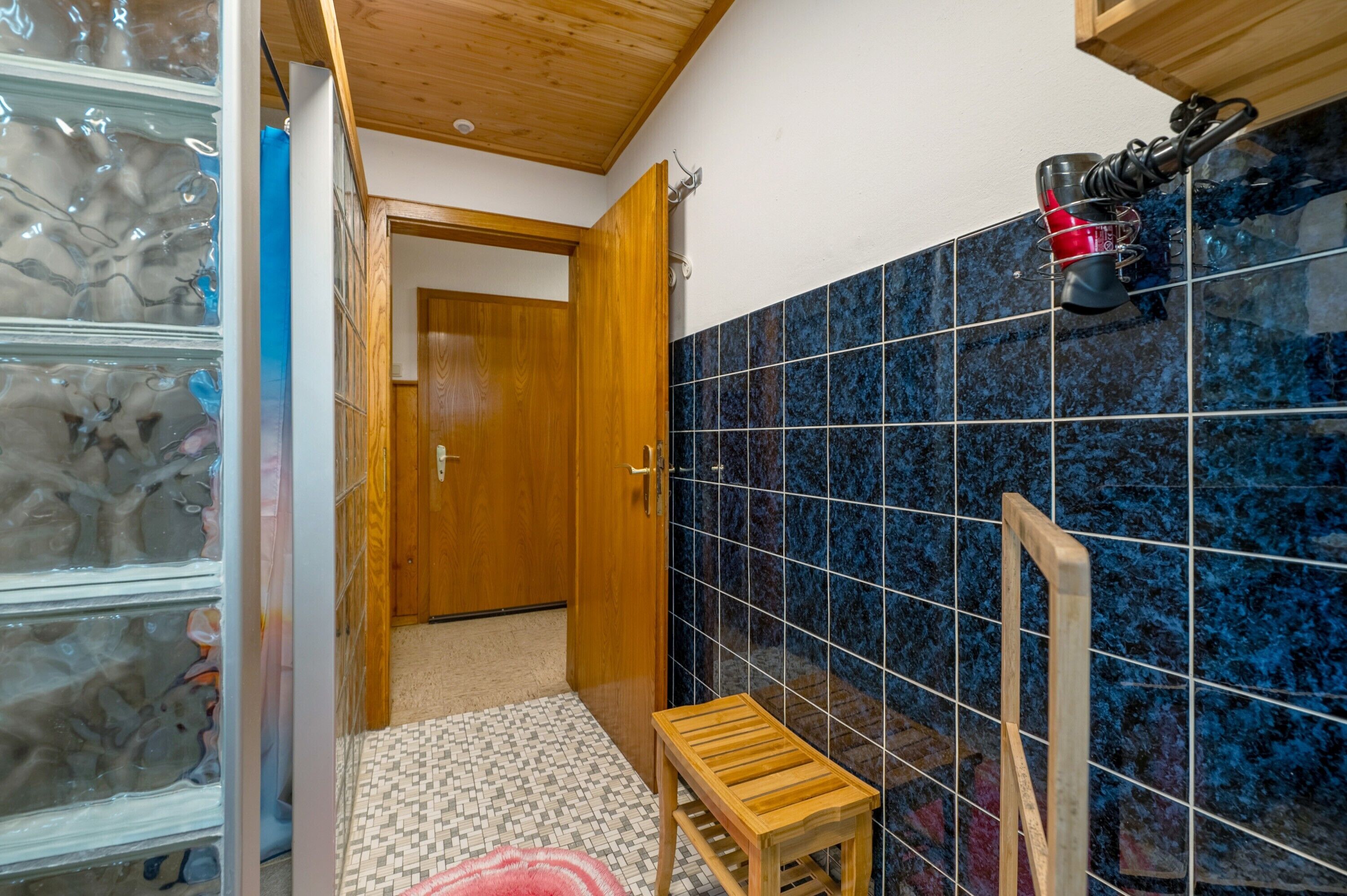 Un baño con puerta de madera, piso de baldosas y un pequeño taburete de madera.