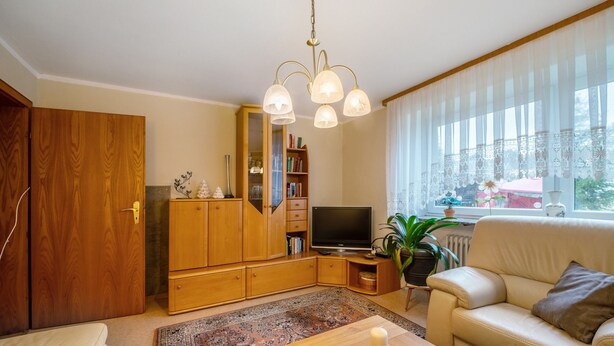 Una sala de estar con un sofá, televisor, mueble de madera, estantería y un amplio ventanal con cortinas.