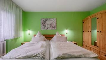 Ein Doppelbett mit weißer Bettwäsche, eine grüne Wand, ein Holzschrank und ein an der Wand befestigtes Kunstwerk.