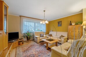 A living room with a television, sofa, coffee table, and a large window with curtains.