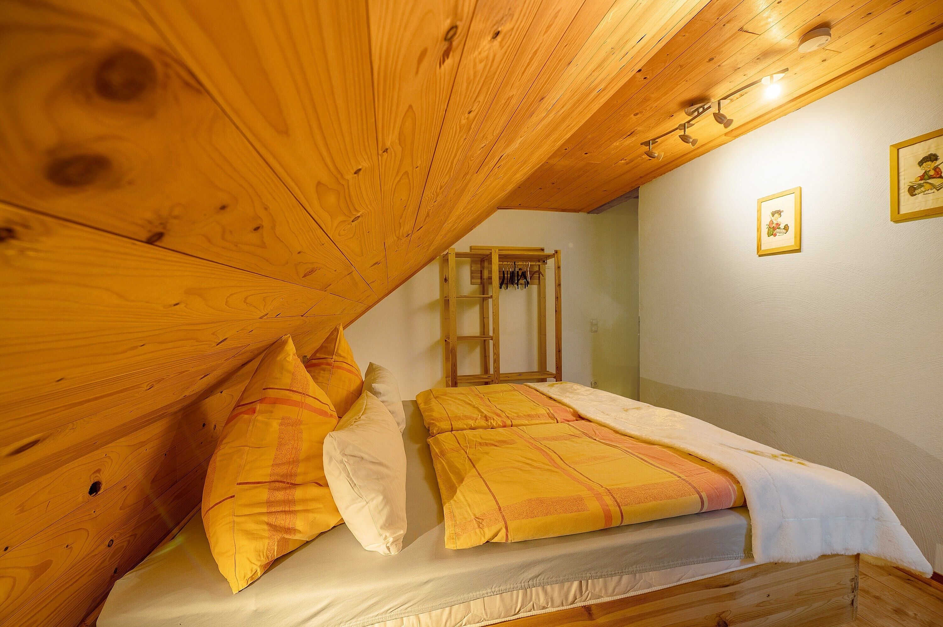 A bedroom with a sloped ceiling, a bed with yellow bedding, and a wooden ladder against the wall.