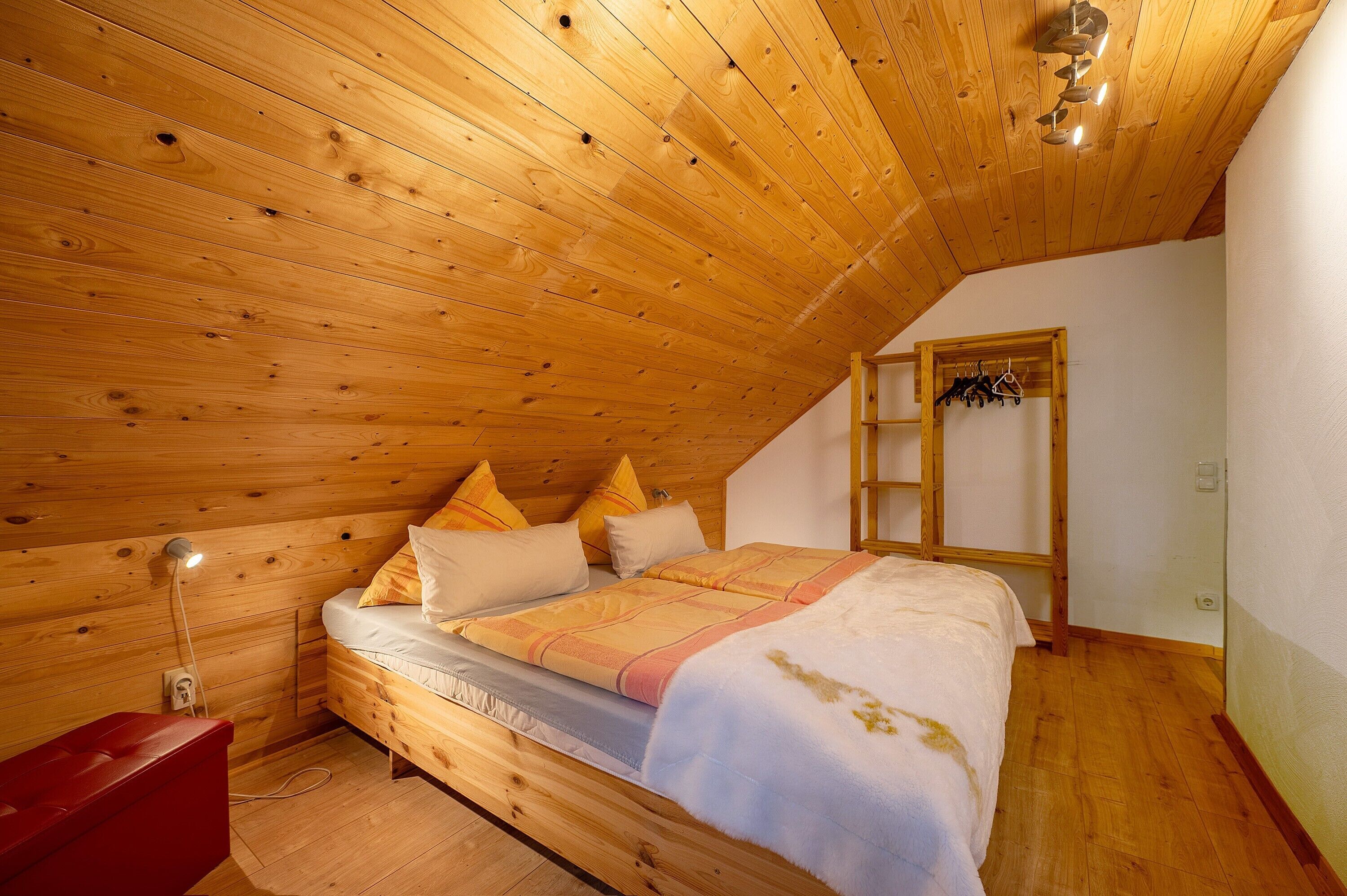 A wooden-paneled room with a bed, a red bench, and a coat rack.