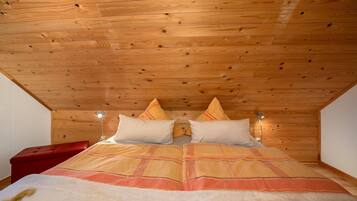 A wooden ceiling, a bed with a blanket, pillows, and a bedside lamp.