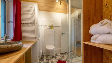 Un baño con lavamanos de piedra, inodoro blanco, ducha y toallero rojo.