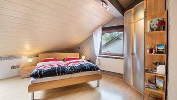 Een slaapkamer met een bed, nachtkastje, een boekenkast en een raam.