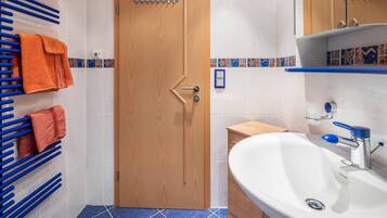 A bathroom with a wooden door, a sink with a blue faucet, and a towel rack with orange towels.