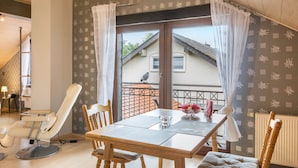Quarto com mesa de jantar, cadeiras, poltrona de massagem e janela com cortinas.