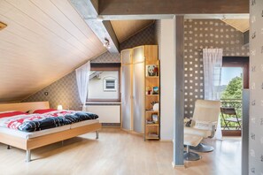 Ein Schlafzimmer mit schrägem Dach, einem Bett, einem Kleiderschrank, einem Stuhl und Blick ins Grüne.
