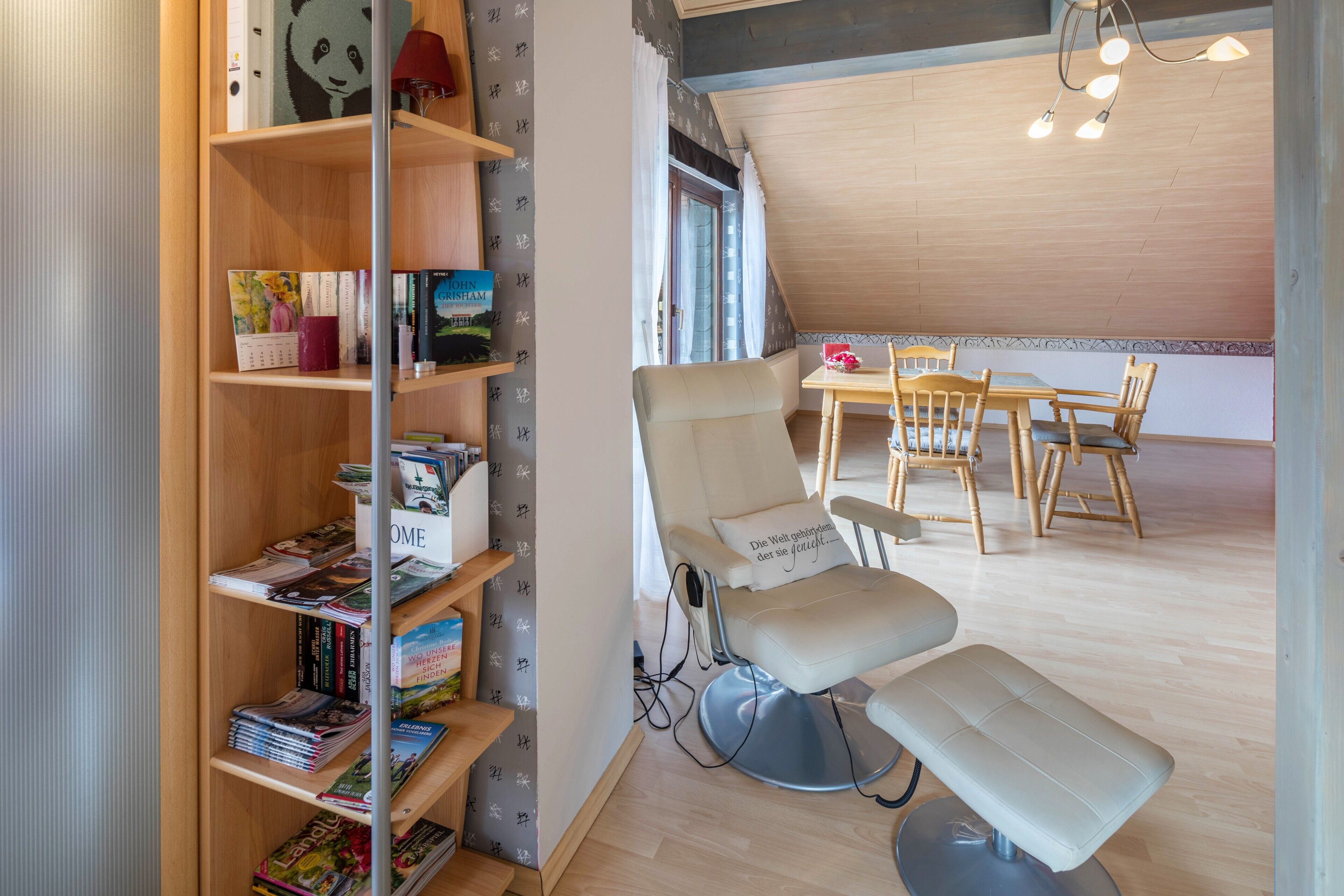 Une pièce comprenant une bibliothèque, un fauteuil de massage, une table à manger avec des chaises et une fenêtre avec des rideaux.