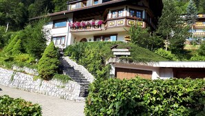 A multi-story building with a balcony, surrounded by greenery and a stone staircase. - Haus Kurparkblick – Apartment Am Schluchtensteig with Wi-Fi (Todtmoos)