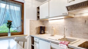 A kitchen with white cabinets, a window with a curtain, a sink, and a coffee maker. - Haus Kurparkblick – Apartment Am Schluchtensteig with Wi-Fi (Todtmoos)