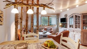 A cozy room with a dining table, chairs, a fruit platter, a television, and a cabinet. - Haus Kurparkblick – Wehratal Apartment with Private Terrace and Wi-Fi (Todtmoos)