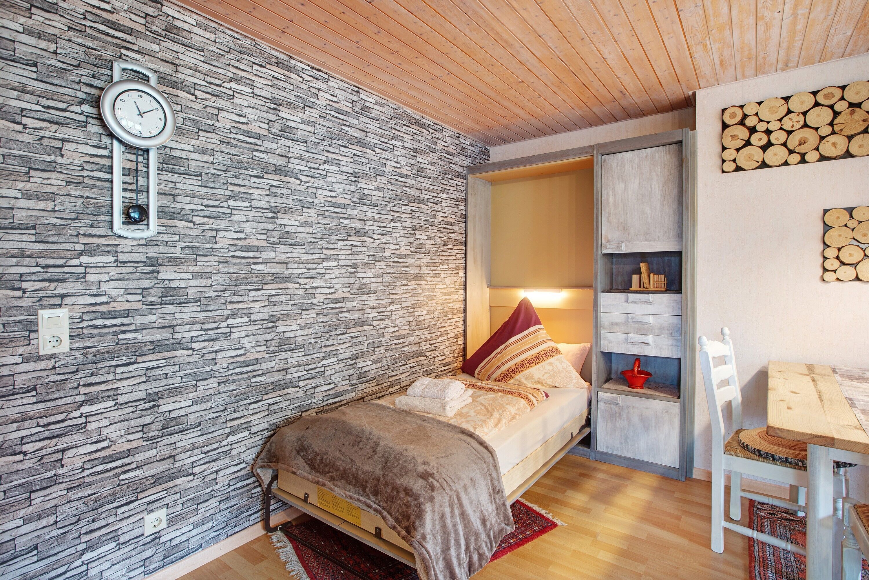 Una camera da letto con parete in pietra, un letto con testiera in legno, un comodino, una sedia e una sveglia.