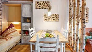 A dining area with a wooden table, white chairs, and a wall decorated with wooden logs. - Haus Kurparkblick – Wehratal Apartment with Private Terrace and Wi-Fi (Todtmoos)