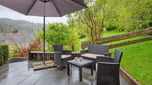 An outdoor patio area with wicker furniture, a table, and an umbrella. - Haus Kurparkblick – Wehratal Apartment with Private Terrace and Wi-Fi (Todtmoos)