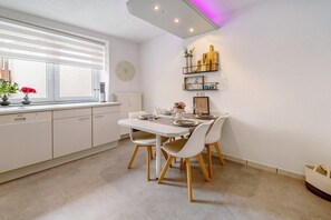 Eine moderne Küche mit Esstisch für vier Personen, wei ßen Schränken und einem Fenster mit Jalousien.