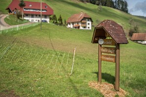 Un panneau indicateur en bois portant les inscriptions « Jorchenhof » et « Familie Singer », un champ herbeux et des maisons en arrière-plan.