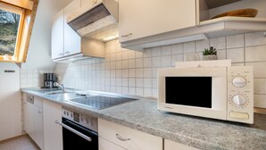 A compact kitchen with white cabinets, a built-in microwave, a stove, and a window. - Apartment Morgensonne, 55 sqm, 2 bedrooms, max. 4 persons (Hofstetten)